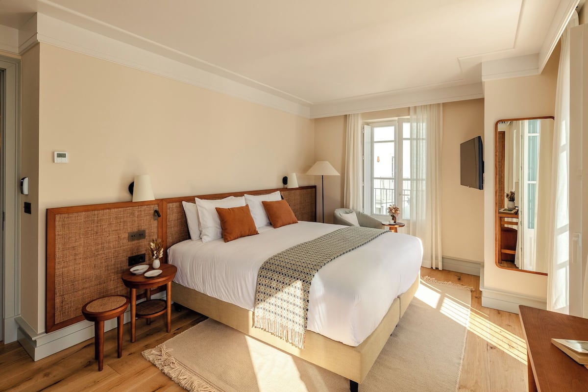 Un dormitorio amplio con una cama grande, mesitas de noche, un espejo y una ventana con cortinas.
