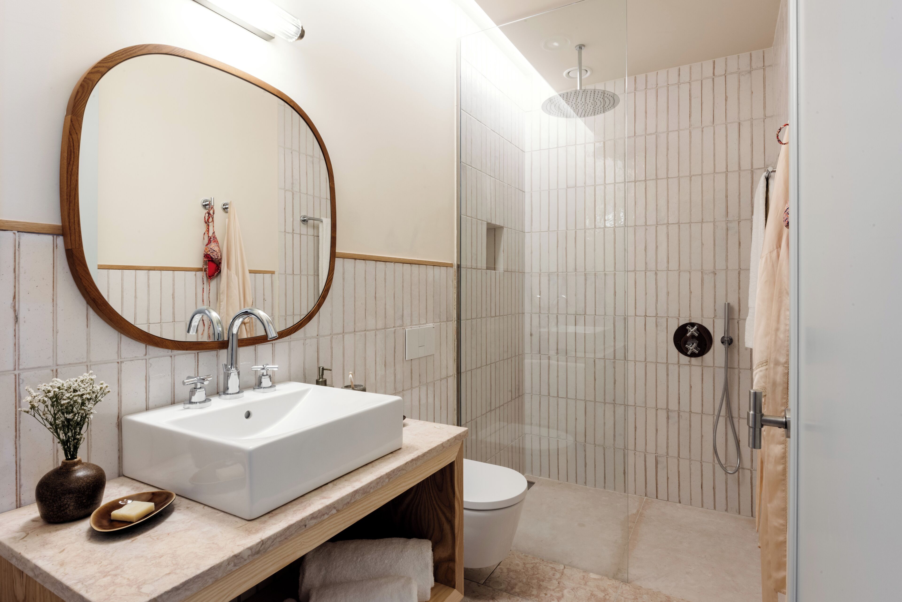 A modern bathroom with a large oval mirror, a rectangular sink, and a glass-enclosed shower.