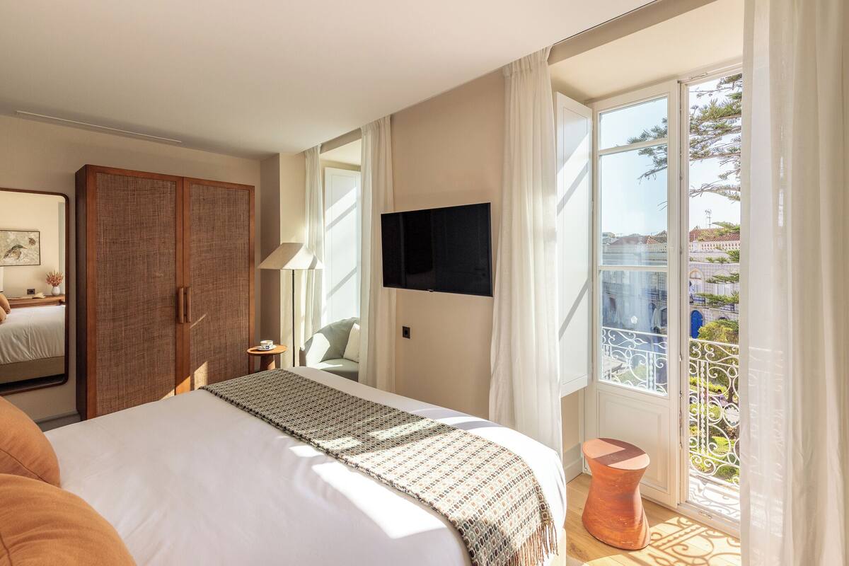 Habitación de hotel con una cama grande, un televisor montado en la pared y un balcón con vistas a la ciudad.