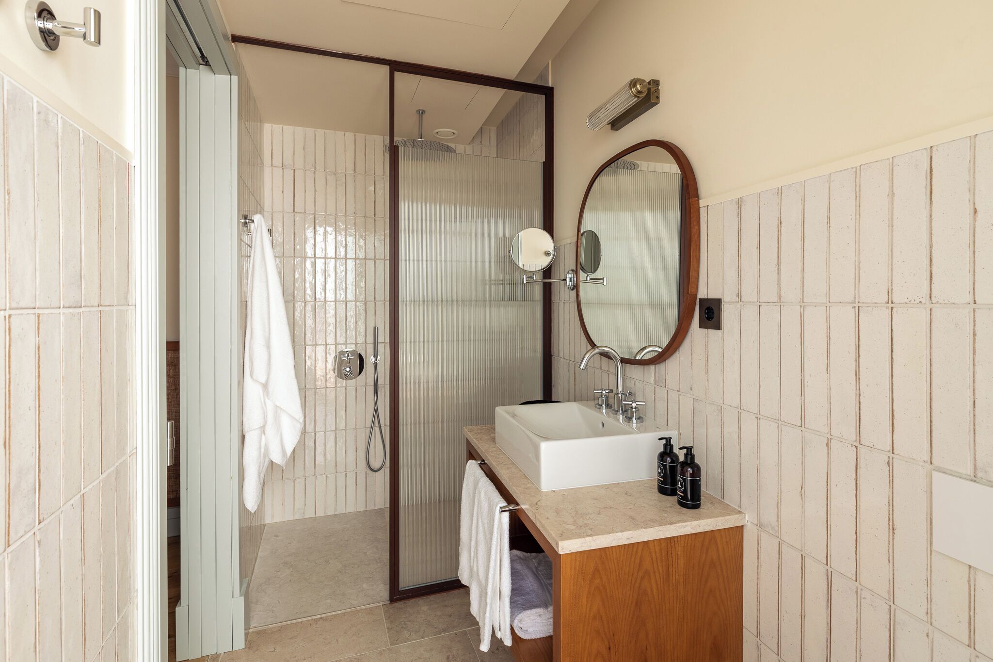 Une salle de bain moderne dotée d’une douche à l’italienne, d’un grand miroir et d’un lavabo avec des articles de toilette.