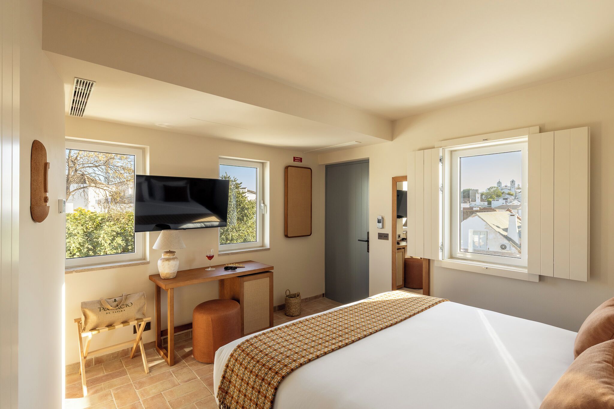 Un dormitorio con una cama, un escritorio, un televisor y un ventanal con vista a la ciudad.