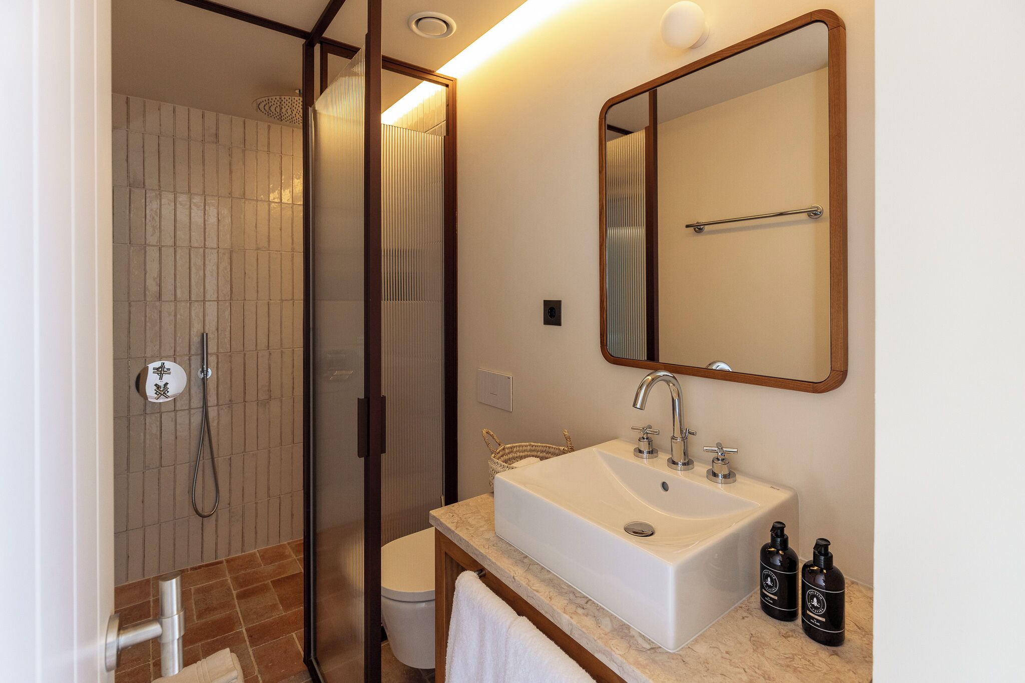 Un baño moderno con cabina de ducha, un lavabo con espejo y dos botellas de artículos de tocador.