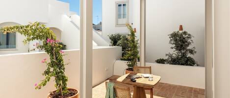 A small patio with a round table and chairs, surrounded by white walls and potted plants.