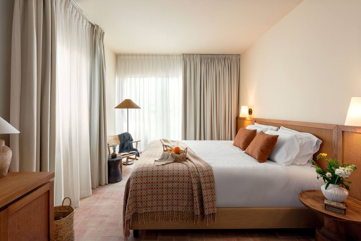 Habitación de hotel con una cama grande, una mesita de noche con lámpara, una silla y una pequeña mesa con un florero.