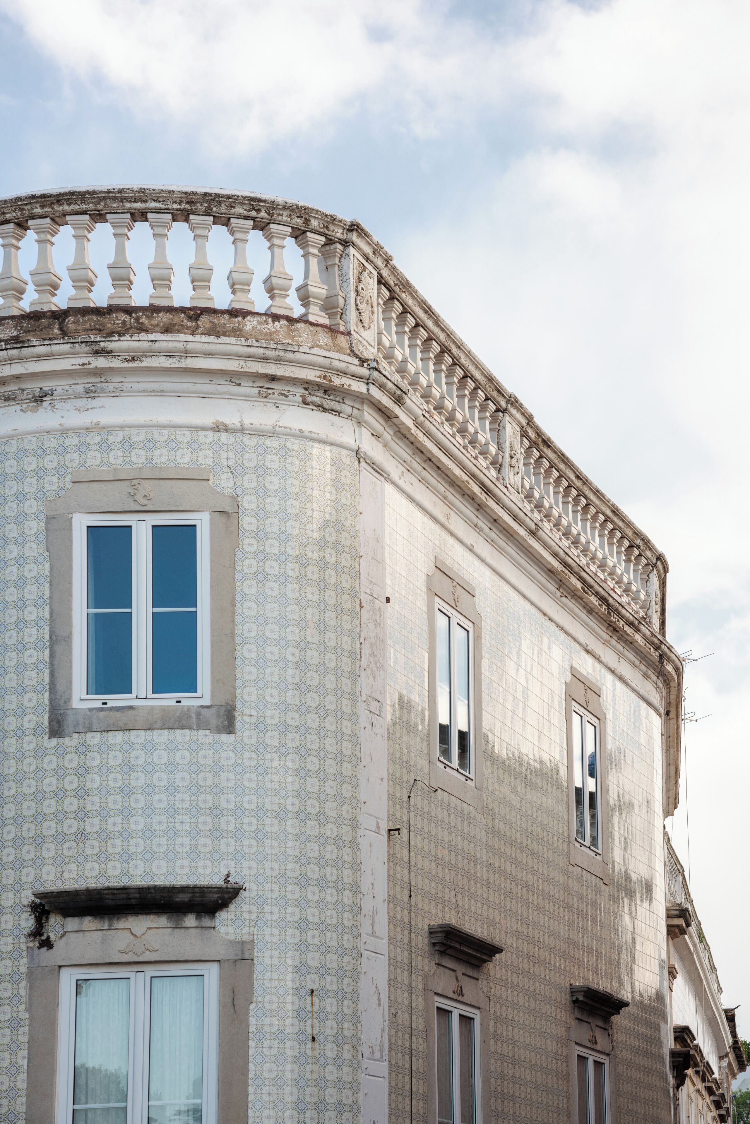 A corner of a building with a patterned facade, a balcony with balustrades, and a window with a white frame.