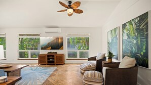 Ein geräumiges Wohnzimmer mit großem Fenster, Deckenventilator, Holzschrank und einem großen Gemälde.