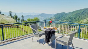 Un balcon avec des fauteuils en osier et une table dressée pour deux personnes, offrant une vue sur un paysage montagneux.