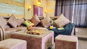 L’intérieur d’un chalet confortable, avec des murs en bois, des fauteuils moelleux, une table basse en verre, une guitare et un jeu d’échecs.