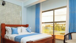 A bedroom with a wooden bed, a view of greenery through a large window, and a chair by the window. - Shanvilla Resort Ltd (Maragua)