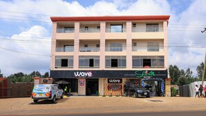 A multi-story building with a 'Wave' sign, a liquor store, and a parked car. - Shanvilla Resort Ltd (Maragua)