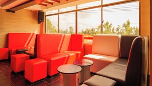 A modern lounge area with red and grey seating, large windows, and a wooden ceiling. - Shanvilla Resort Ltd (Maragua)