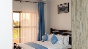 A bedroom with a bed, a window with sheer curtains, a view of greenery outside, and a framed picture on the wall. - Shanvilla Resort Ltd (Maragua)