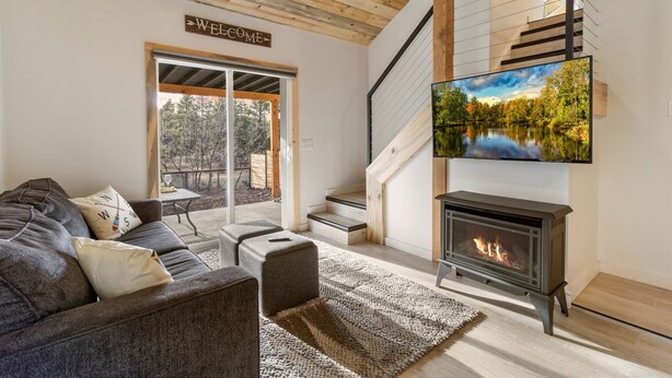 Una sala de estar moderna con chimenea, un sofá, un televisor montado sobre la chimenea y una escalera que conduce a un nivel superior.