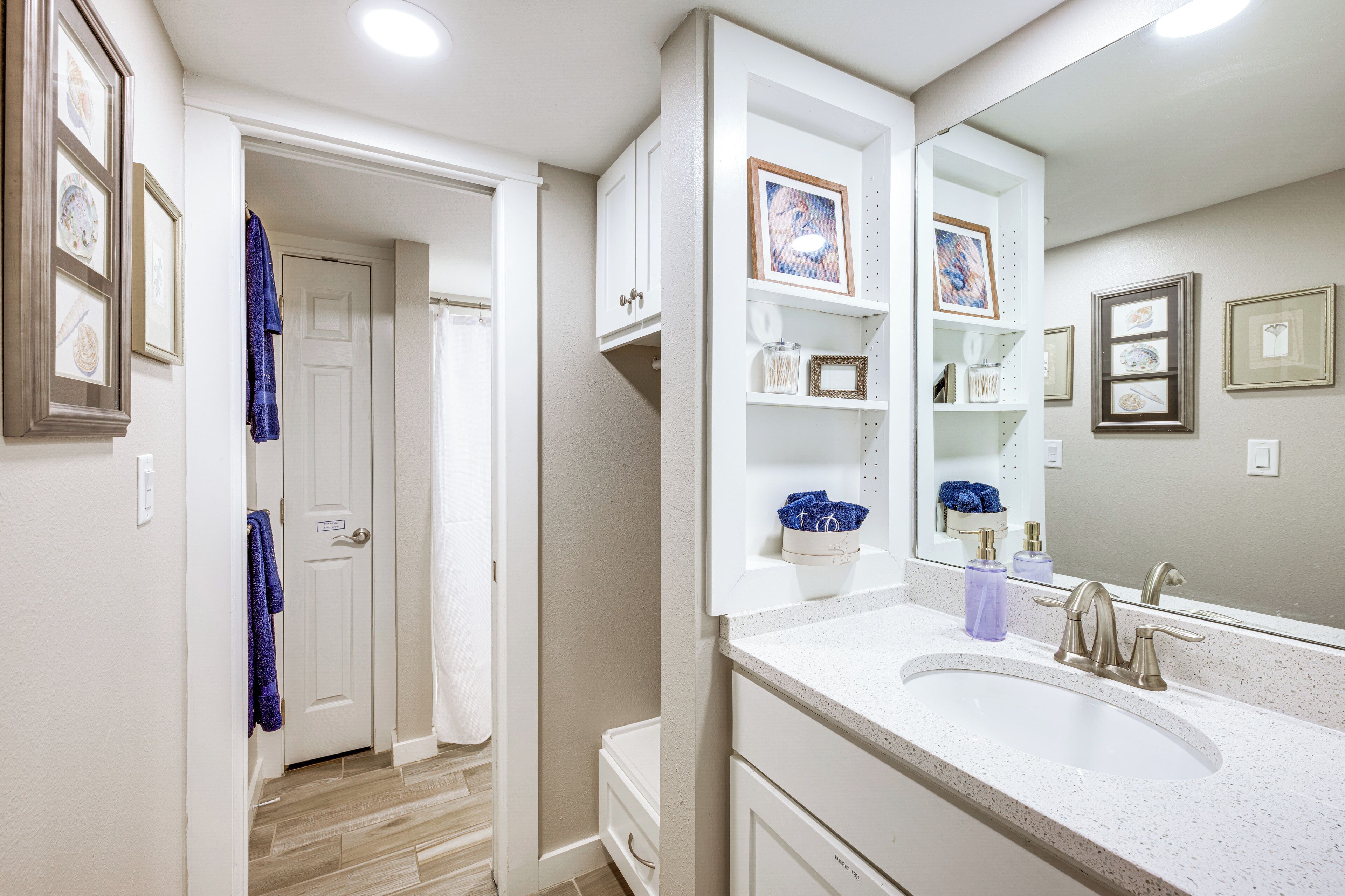 A bathroom with a white vanity, a large mirror, and framed pictures on the wall.