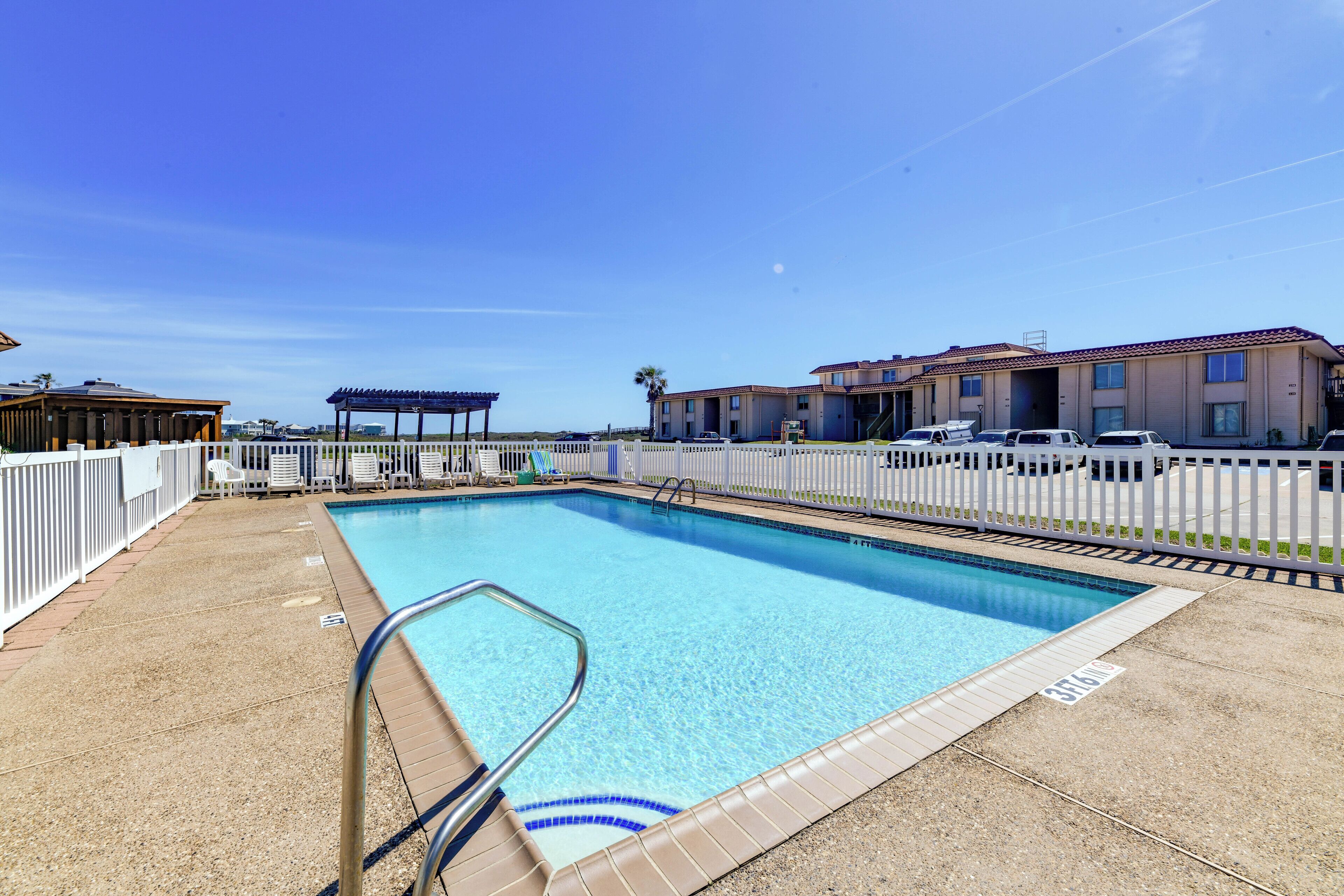 A swimming pool with a clear blue water, a white fence, and a covered seating area.