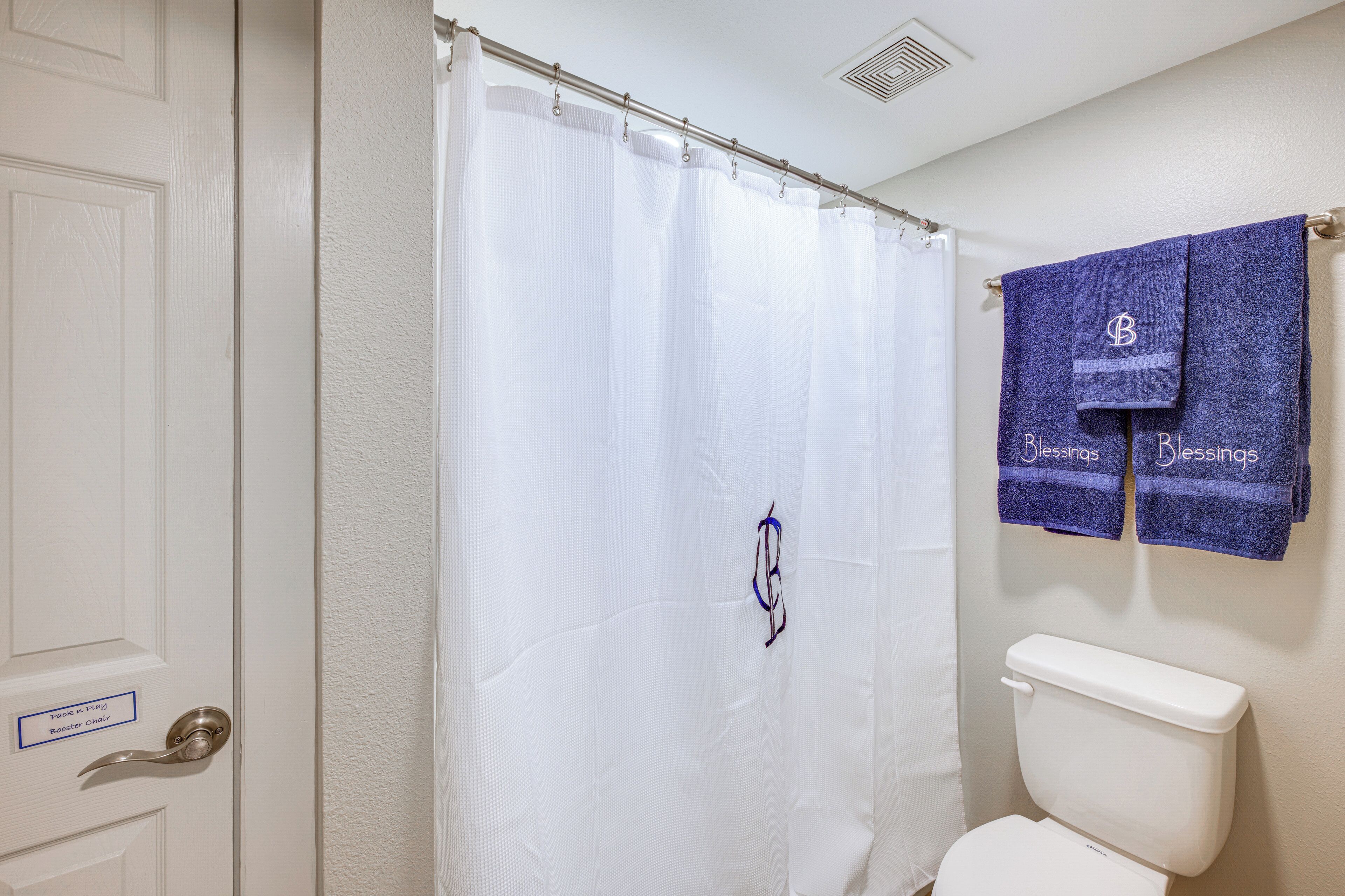 A bathroom with a white shower curtain, a white toilet, and two towels hanging on the wall.
