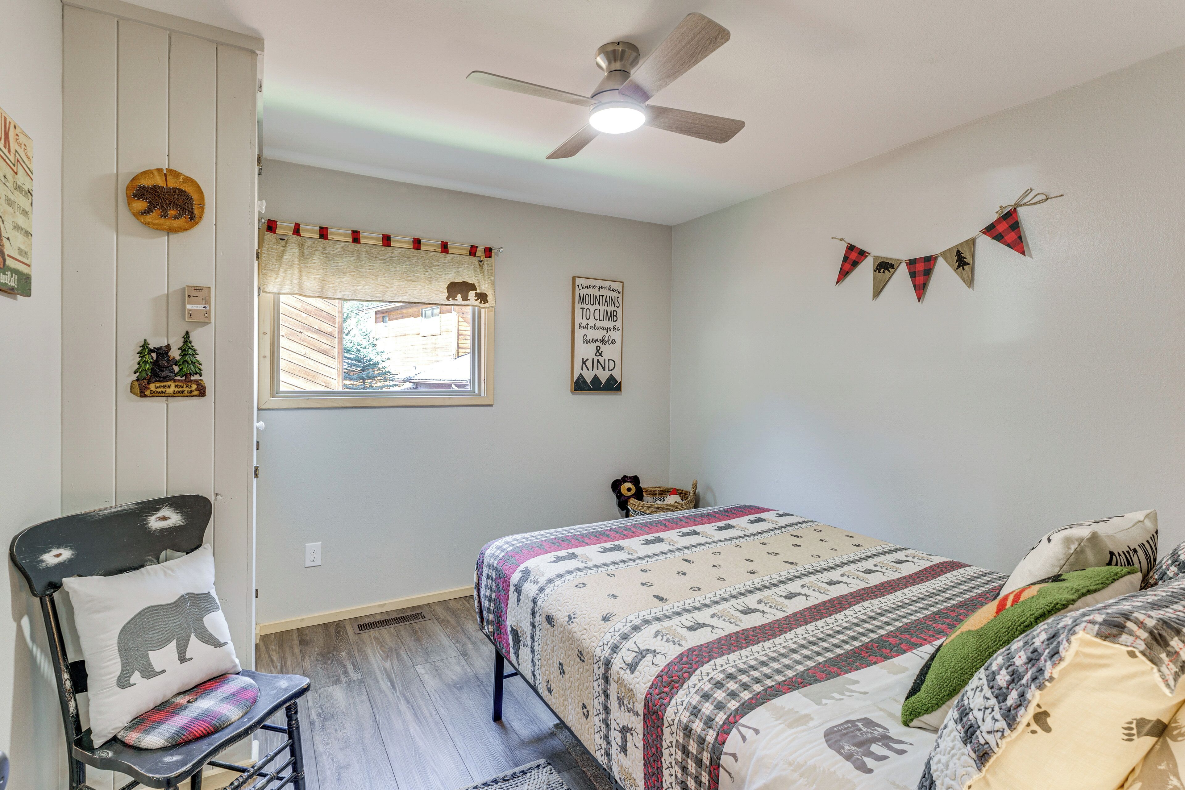 A bedroom with a bed, a chair, a window with a view, a ceiling fan, and wall decorations.