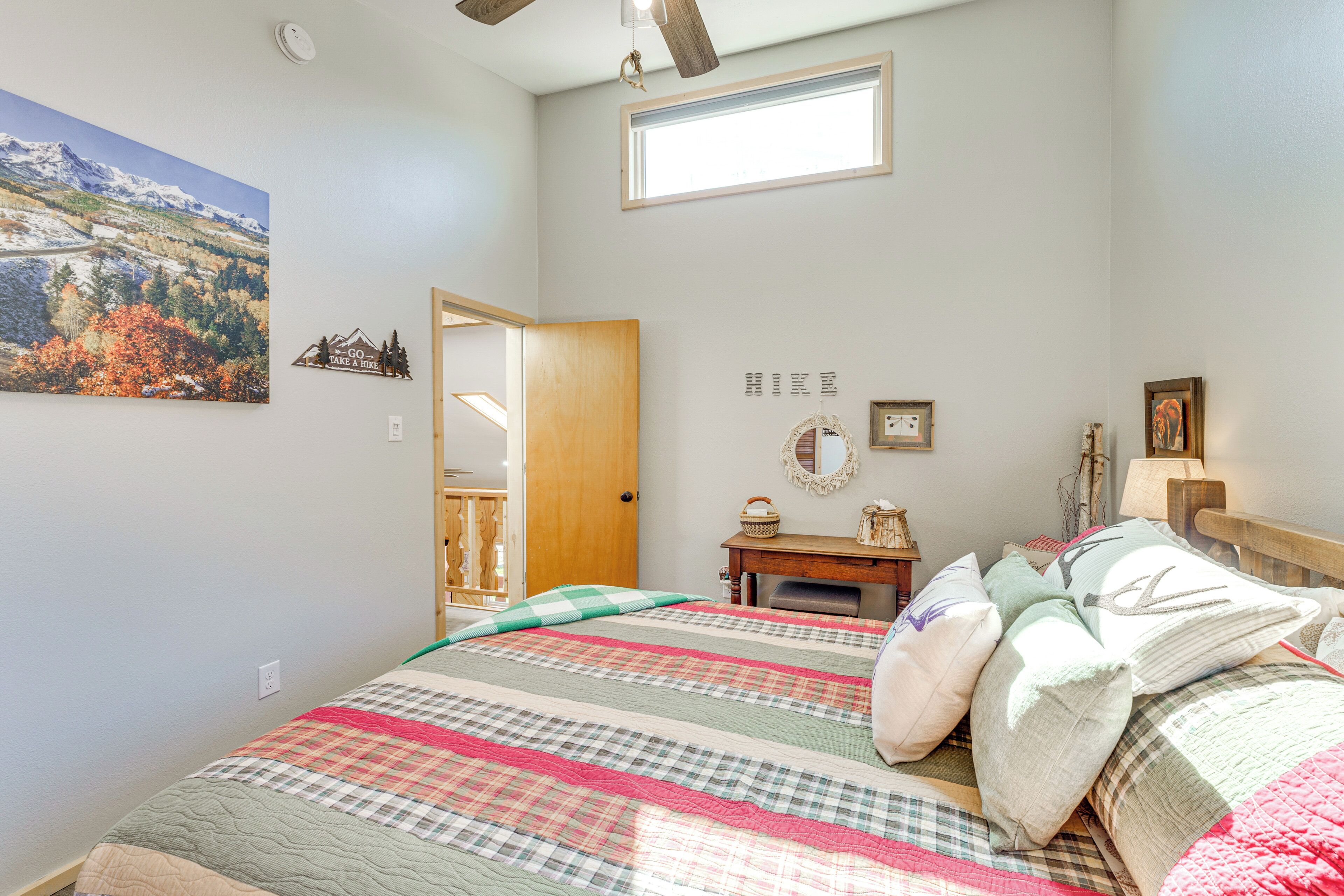 A bedroom with a bed, a window, a door, and a wall with a painting and a sign.