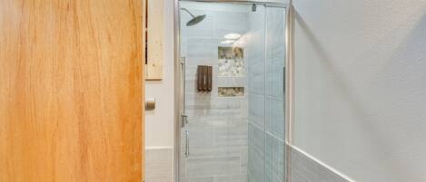 A modern bathroom with a glass shower enclosure, a wooden door, and a tiled floor.