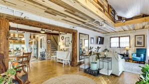 Un salón amplio con suelo de madera, una alfombra grande y una variedad de muebles, incluyendo un sofá, sillas y una mesa de comedor.