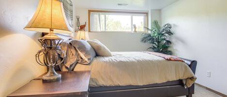 A bedroom with a bed, a nightstand, a lamp, a window, and a plant.
