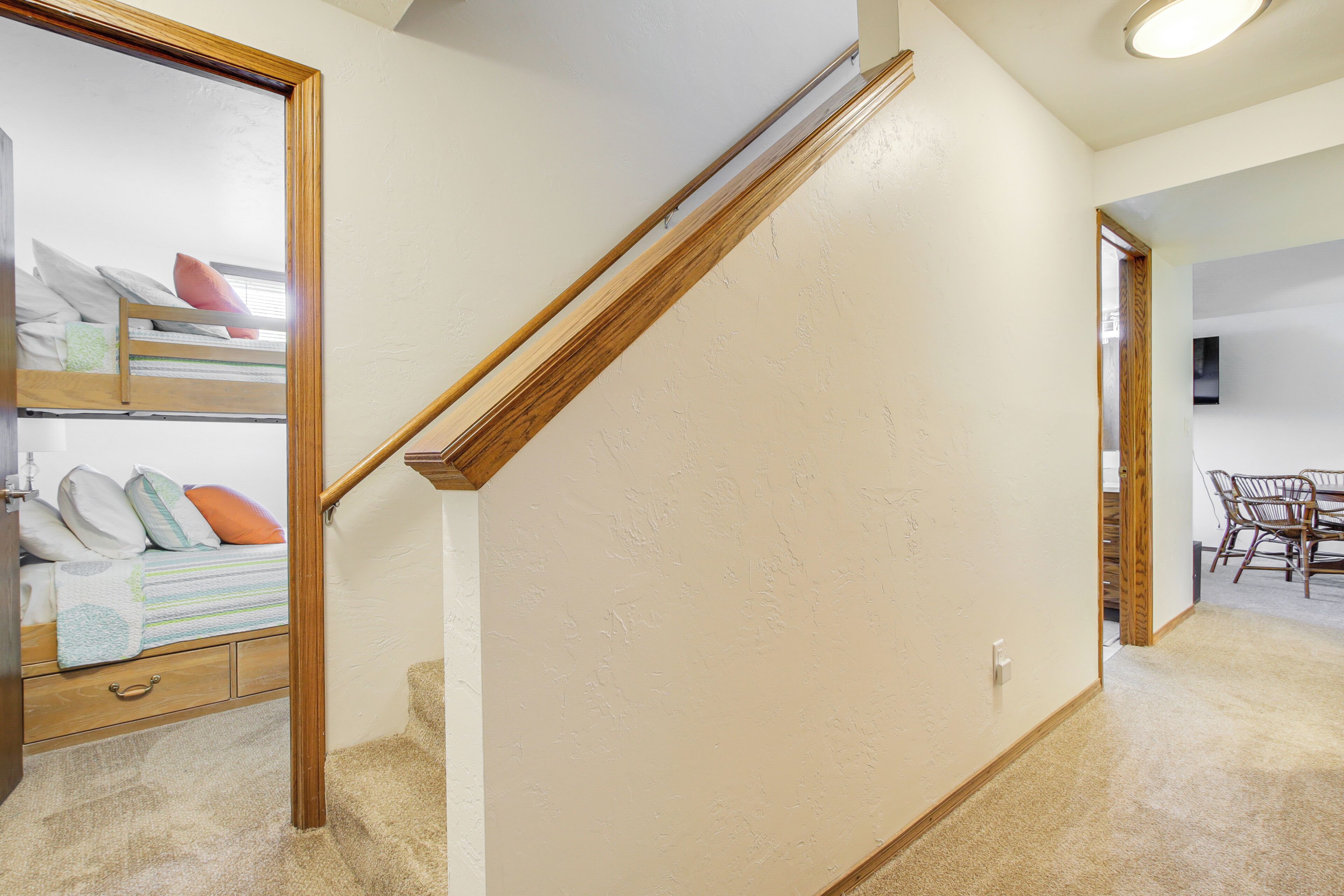A staircase with a wooden handrail leading to a bedroom with a bed, a nightstand, and a dresser.