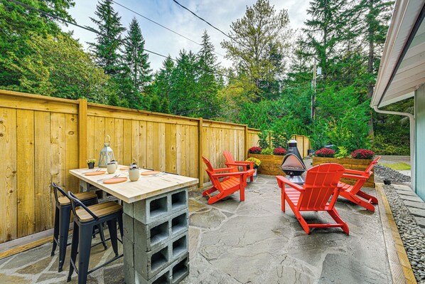 An outdoor patio with a wooden table and chairs, a stone floor, and a wooden fence. - Pet-friendly Studio w/ Fire Pit in Olympia! (Olympia)