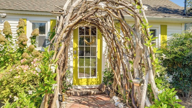 Una casa gialla con un arco coperto di vite che conduce a una porta.