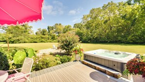 Un patio con una vasca idromassaggio, sedie in vimini e un ombrellone rosa.