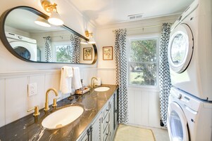 Un baño con lavamanos doble, un espejo grande, lavadora y ventana con cortinas estampadas.