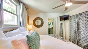 Camera d'albergo con un letto grande, una ventola a soffitto, una TV e un bagno visibile attraverso una porta aperta.