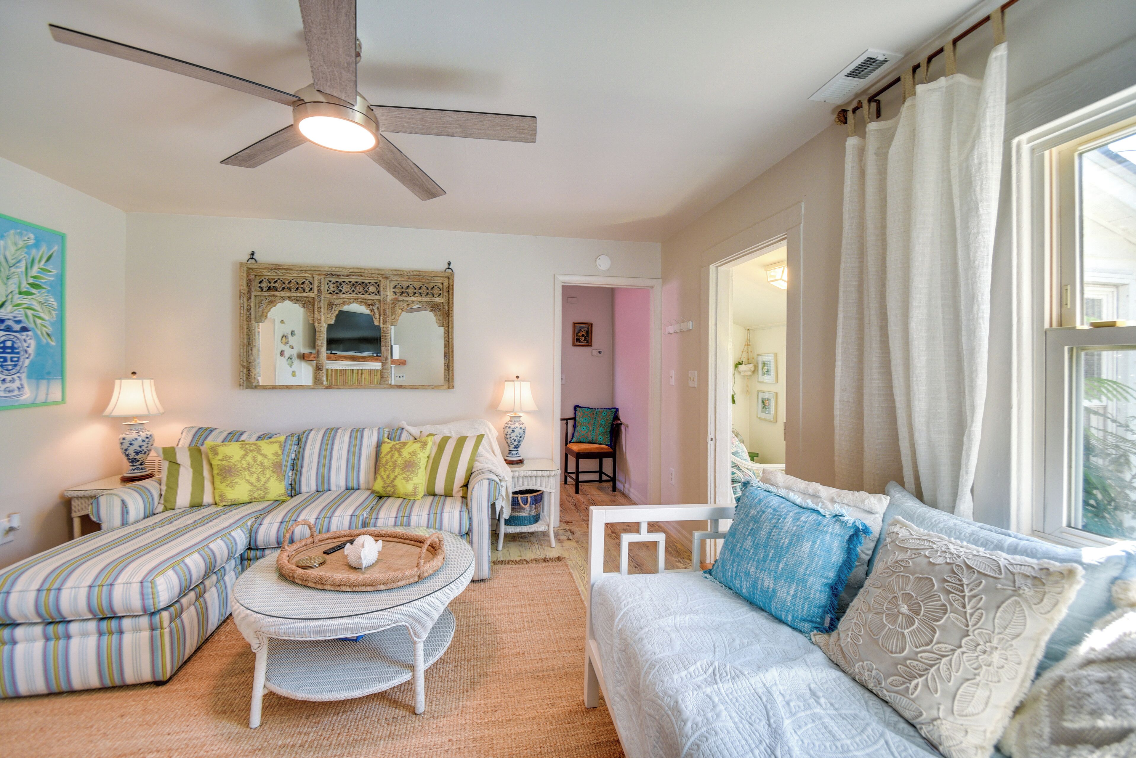 A living room with striped sofas, a ceiling fan, and a view of the outside.