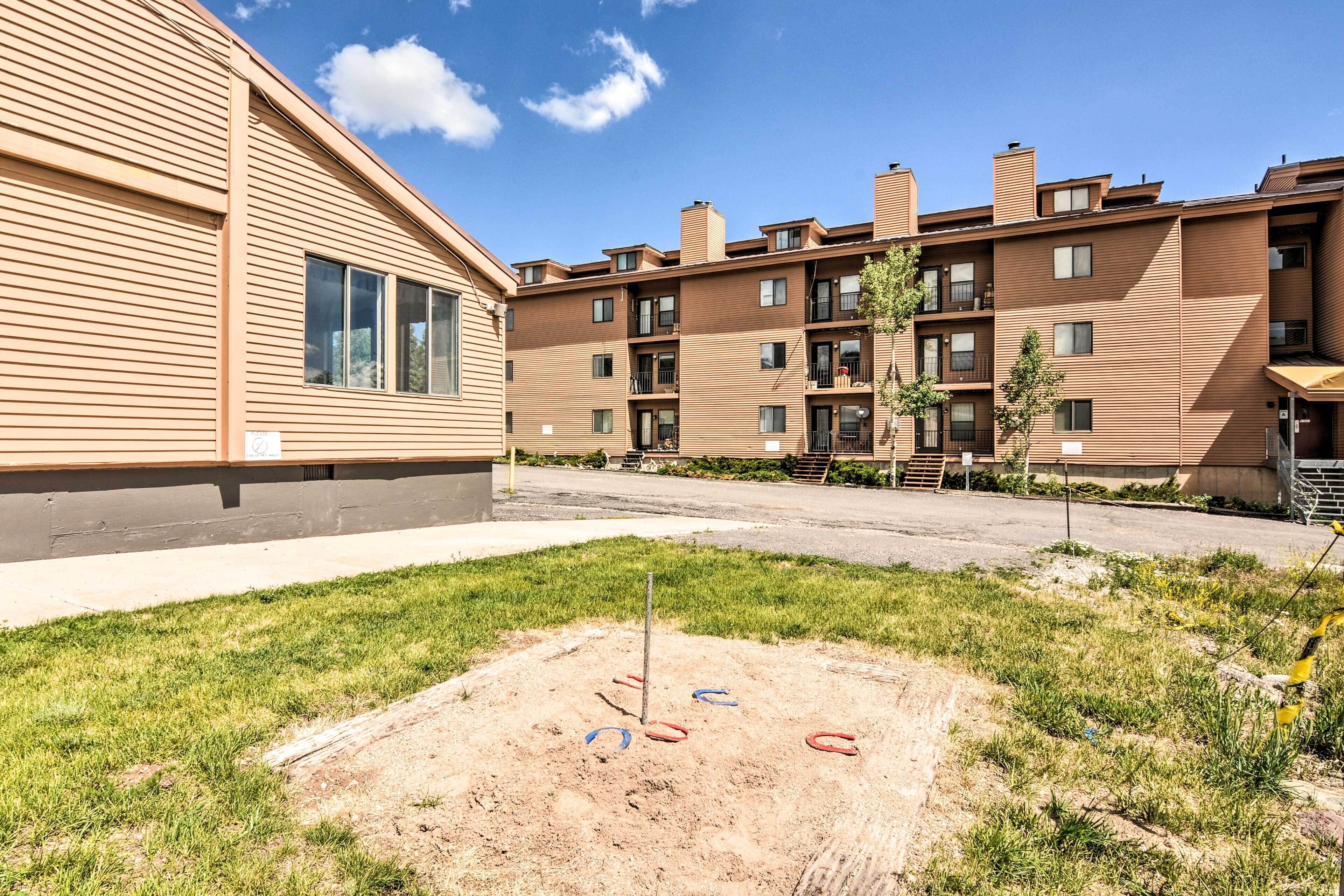 Un edifici residencial de diversos pisos amb teulada plana, un pati enjardinat i una zona de jocs amb cadira d'oscil·lació i tobogan.