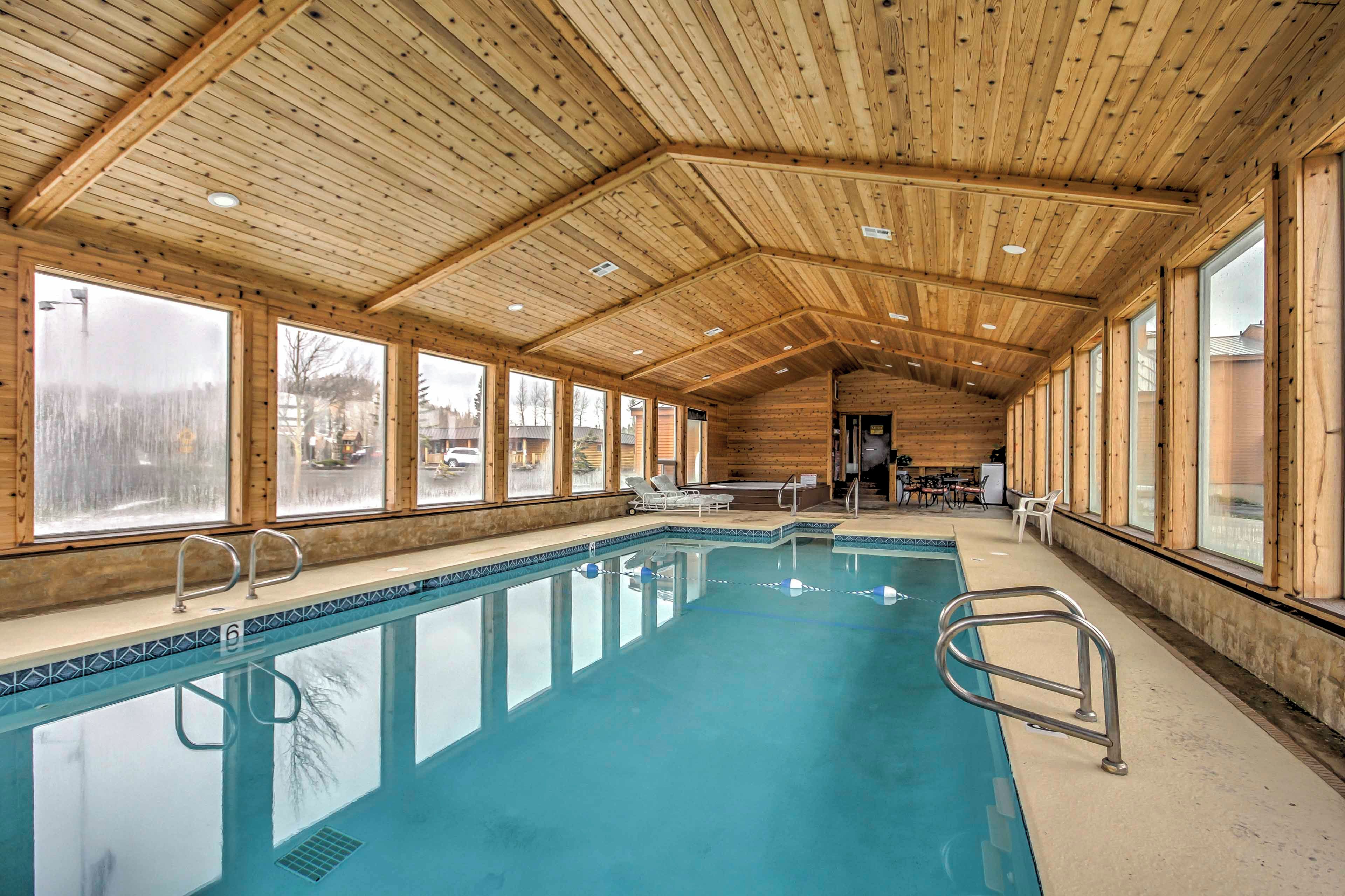 An indoor swimming pool with clear windows, wooden ceiling, and a view of the outside.