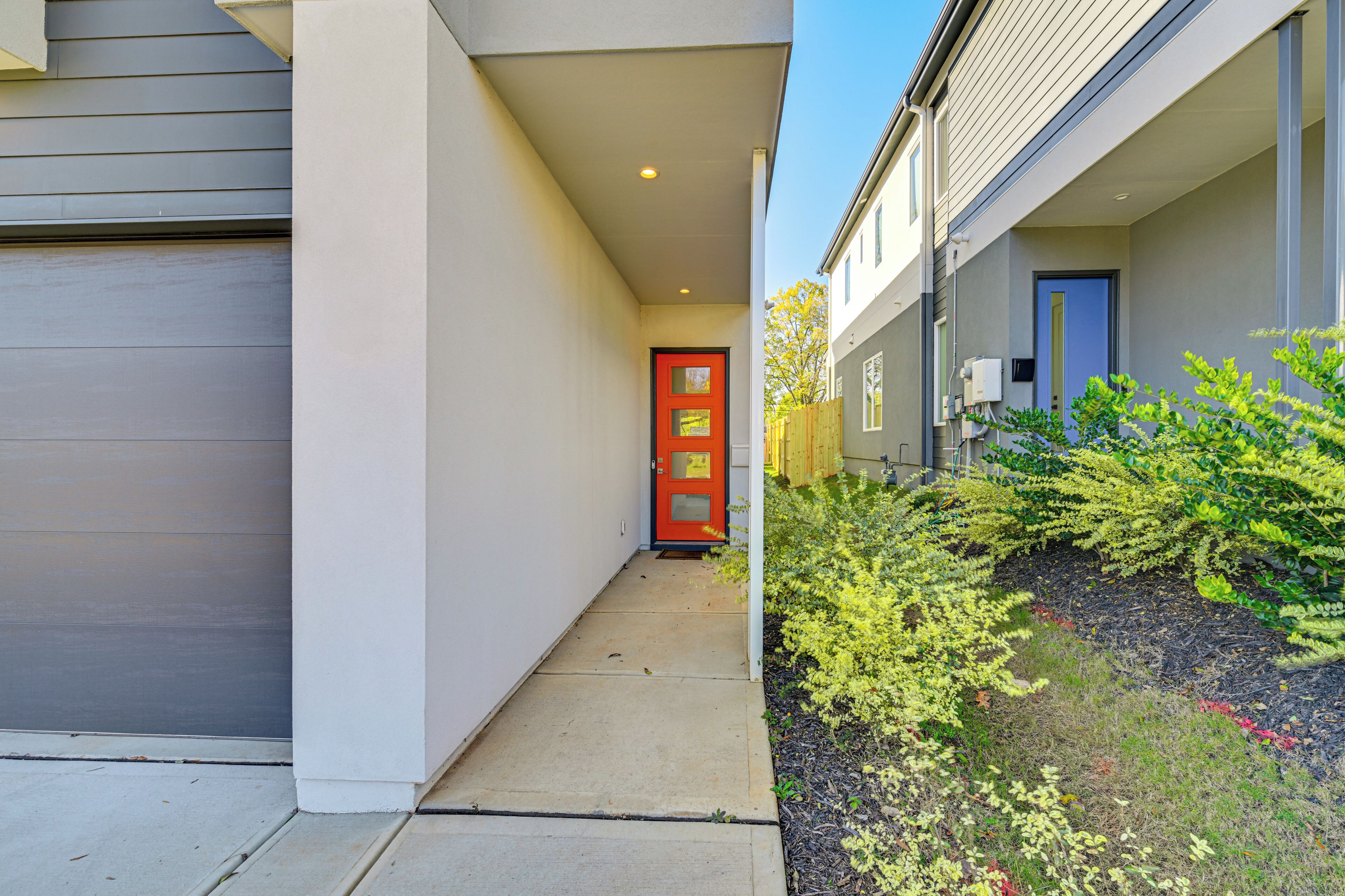 A narrow pathway leading to a red door with a small window, flanked by white walls and a grey garage door.