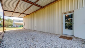 Un espace extérieur abrité, doté d’un sol en gravier, d’un toit en métal et d’un bâtiment blanc avec une porte.