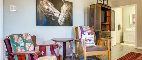 Un salón con una mecedora, una mesa de madera y un cuadro de caballos en la pared.
