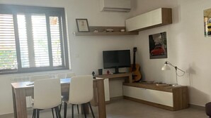 A modern living room with a dining area, a TV, a guitar, and a sofa.