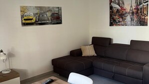 A modern living room with a brown sectional sofa, a wooden dining table with chairs, and two paintings on the walls.