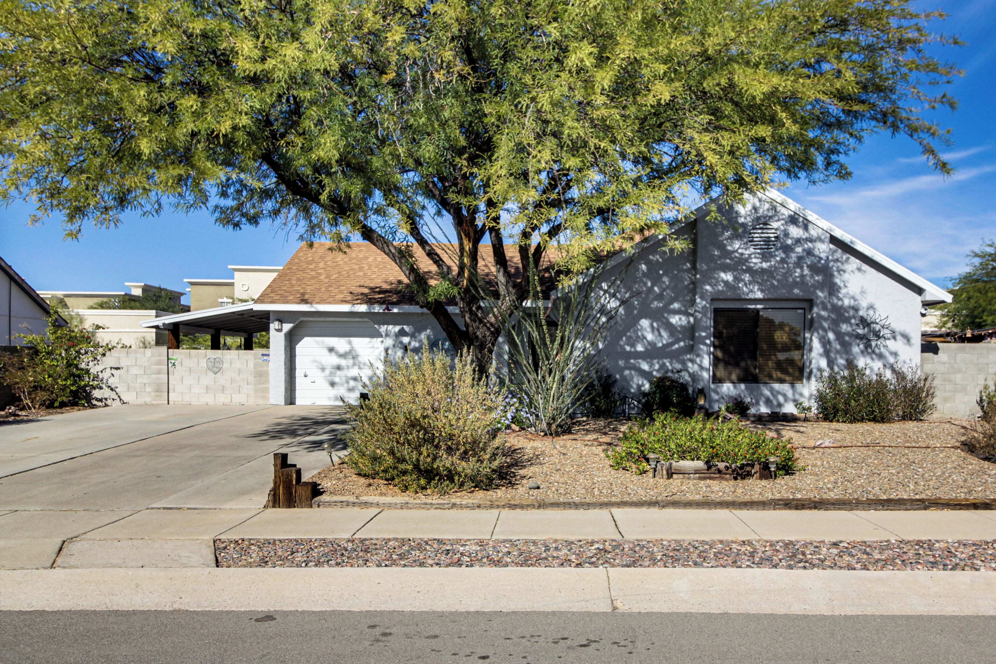 Ein Wohnhaus mit Garage, Auffahrt und einem gepflegten Garten mit verschiedenen Sträuchern und einem Baum, der Schatten spendet.