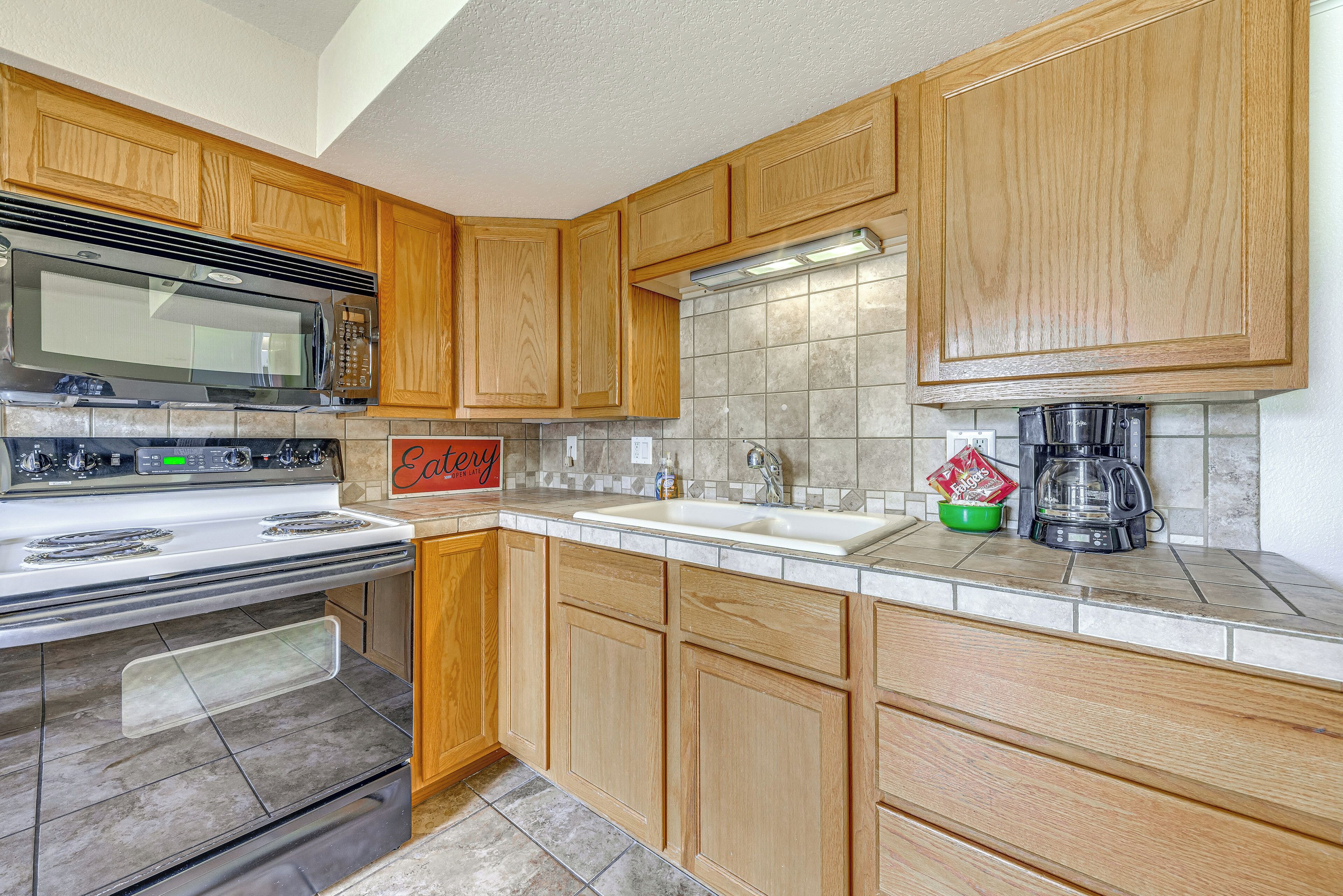 A kitchen with wooden cabinets, a stainless steel stove, a microwave, a sink, and a coffee maker.