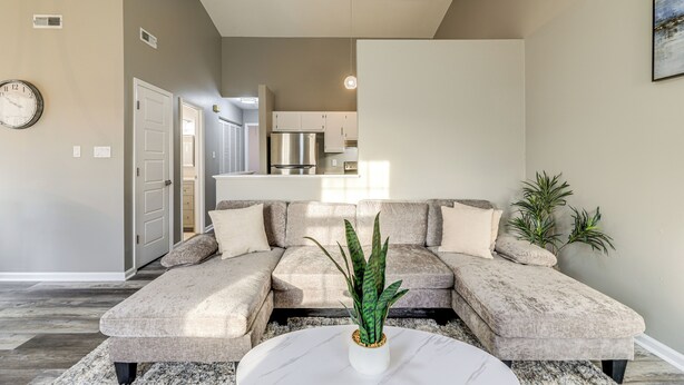 A modern living room with a sectional sofa, a coffee table with a plant, and a kitchen in the background.