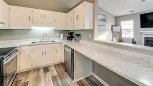 A modern kitchen with white cabinets, a marble countertop, and a built-in dishwasher.