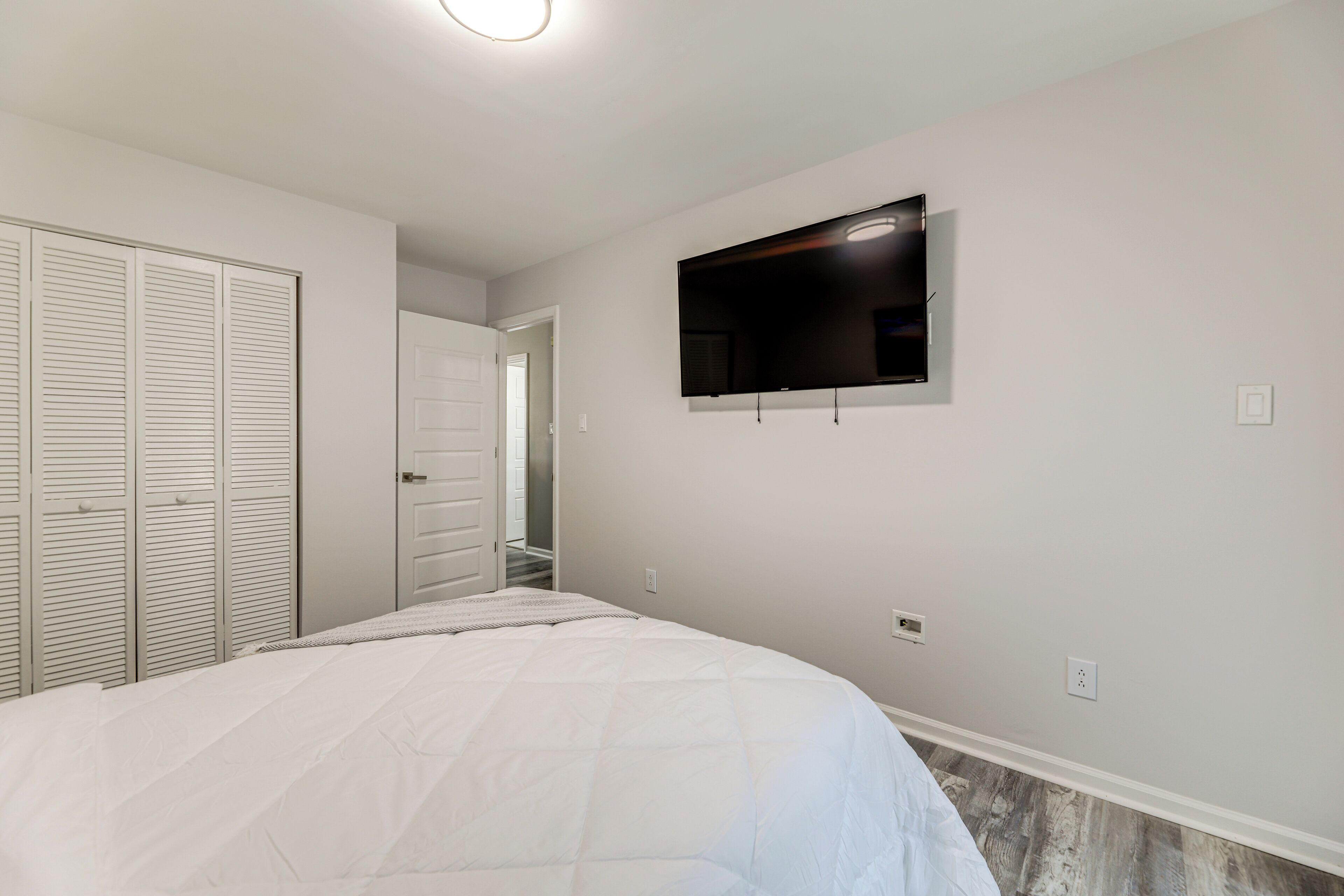 A bedroom with a bed, a TV mounted on the wall, and a closet.