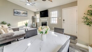 A modern living room with a marble dining table, grey sofas, a white vase with flowers, a ceiling fan, and a fireplace.