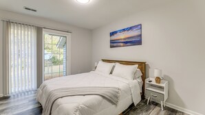 A bedroom with a large bed, a nightstand, a painting, and a view through the window.