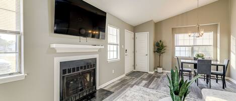 A spacious living area with a fireplace, a mounted TV, and a dining area with a table and chairs.