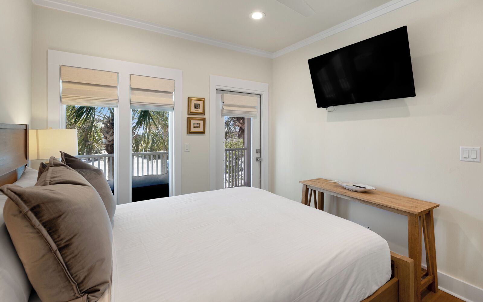 A bedroom with a large bed, a TV mounted on the wall, and a balcony with a white railing.