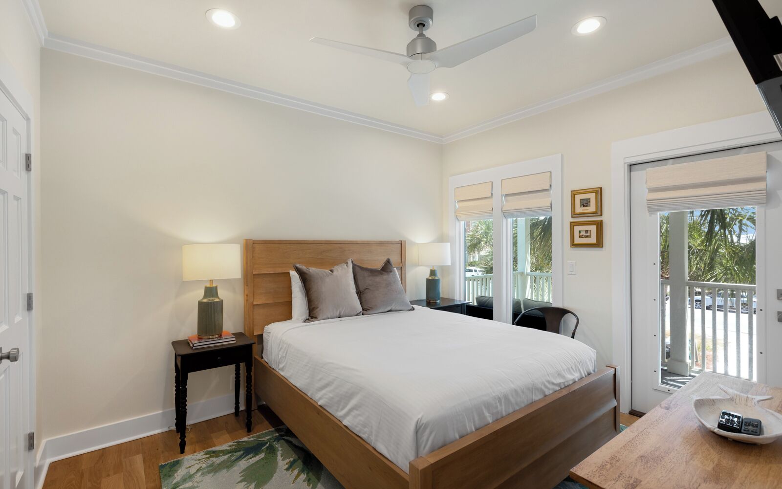 A bedroom with a bed, bedside tables, a ceiling fan, and a view of the outside.