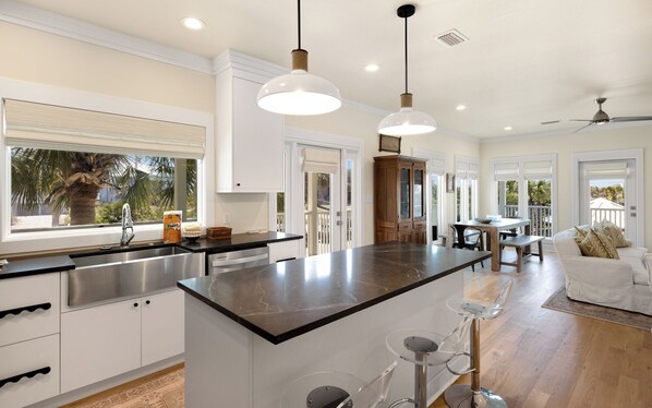A modern kitchen with a large island, pendant lighting, and a view of the outdoors.